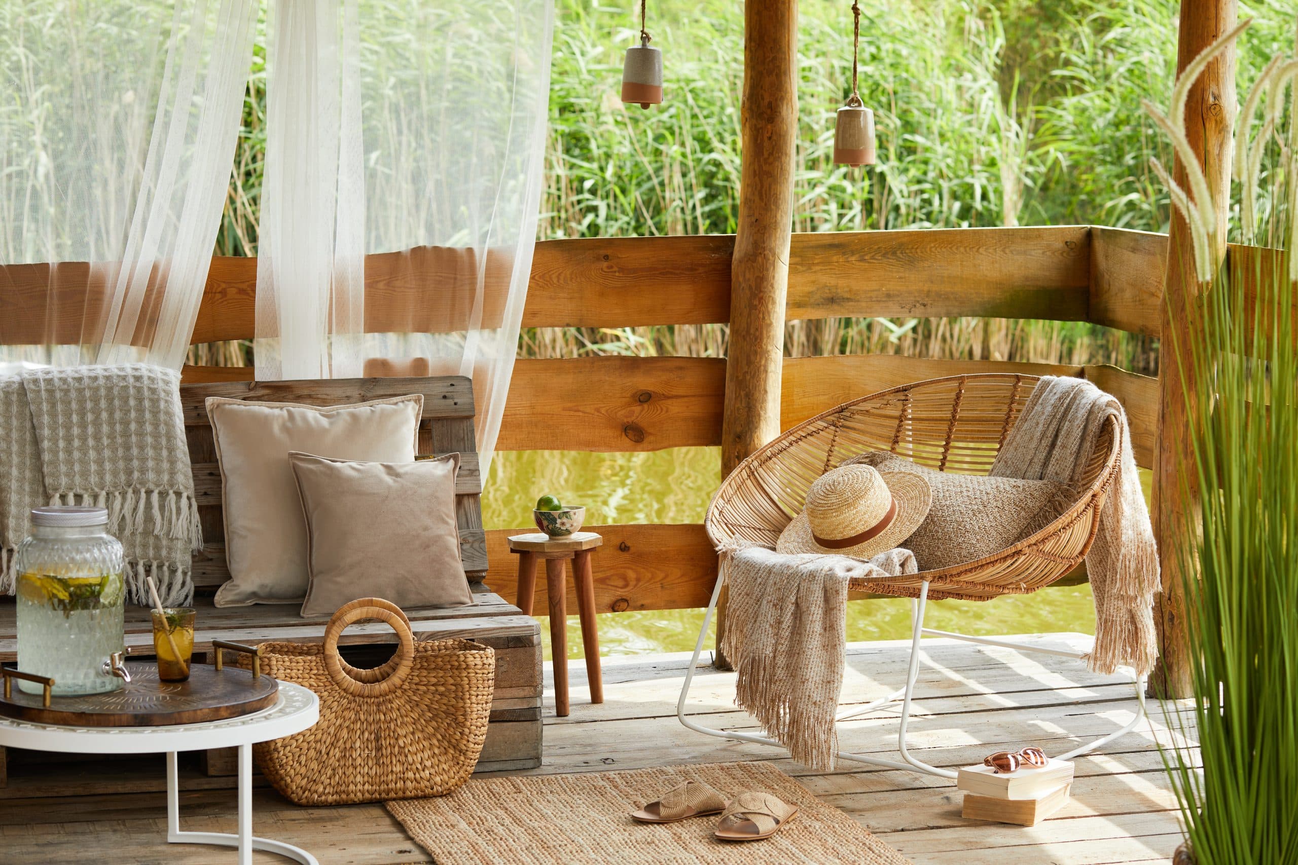 Interior design of  summer gazebo by the lake with stylish rattan armchair, coffee table, sofa, pillows, plaid and elegant accessories in modern decor. Summer vibes.